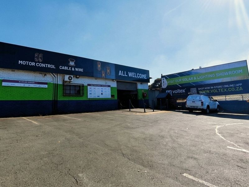 Front exterior view of a commercial mixed-use property featuring a paved parking area, painted brick facade, and prominent signage for a solar and lighting showroom.