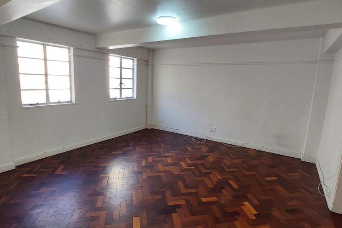 A spacious, empty living room featuring original herringbone parquet timber flooring and large windows providing natural light.