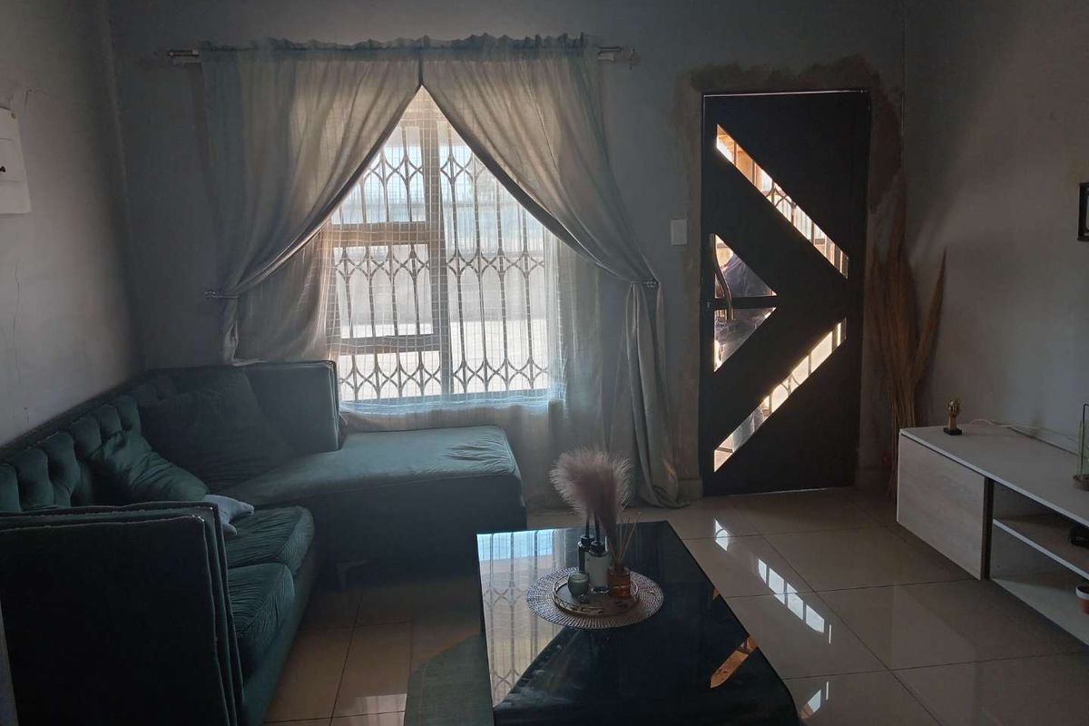 A living room featuring tiled flooring, a window with security bars, and a decorative entrance door with visible unfinished plasterwork around the frame.