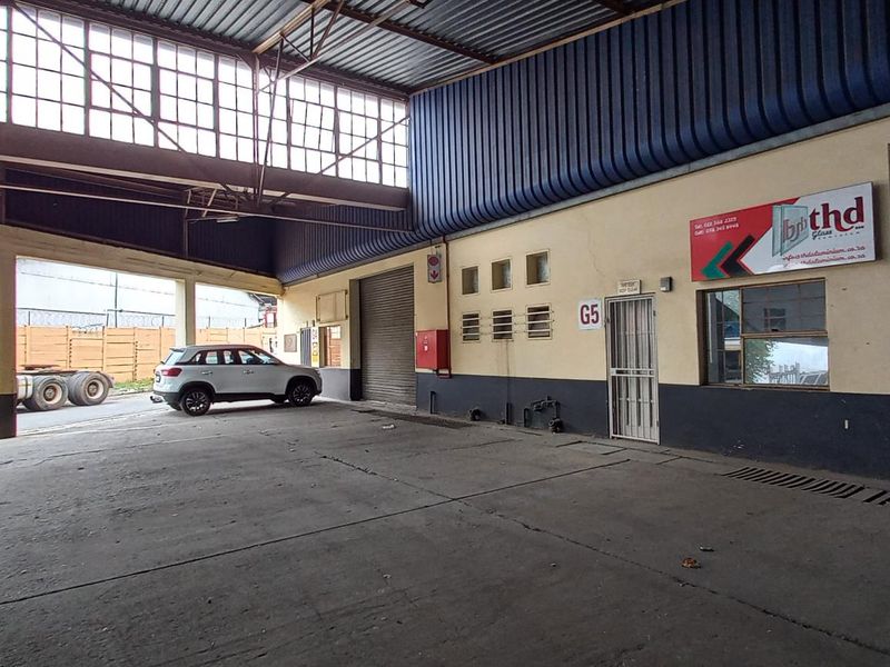 Industrial warehouse unit featuring a large roller shutter door, concrete flooring, and covered loading area with high-clearance metal roof structure.