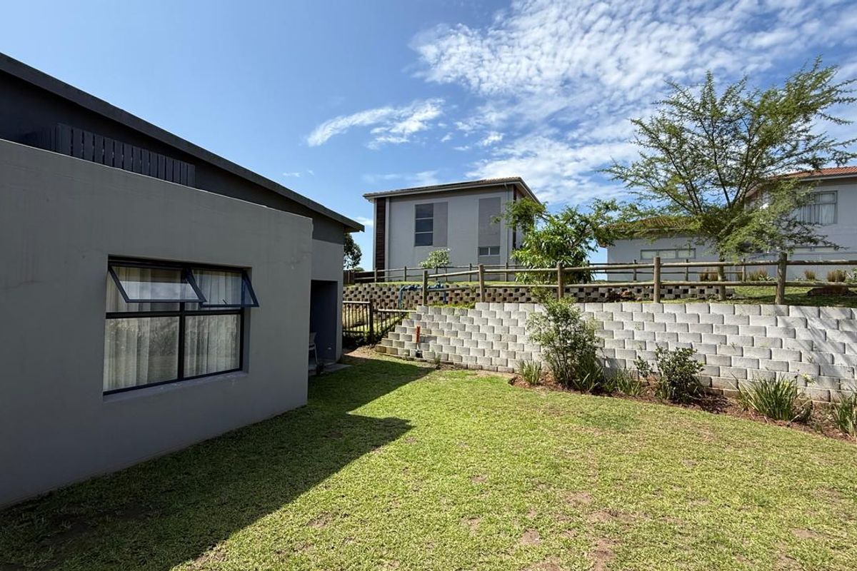 A view of the rear garden area featuring a lawn, retaining wall, and timber fencing, adjacent to the townhouse exterior.
