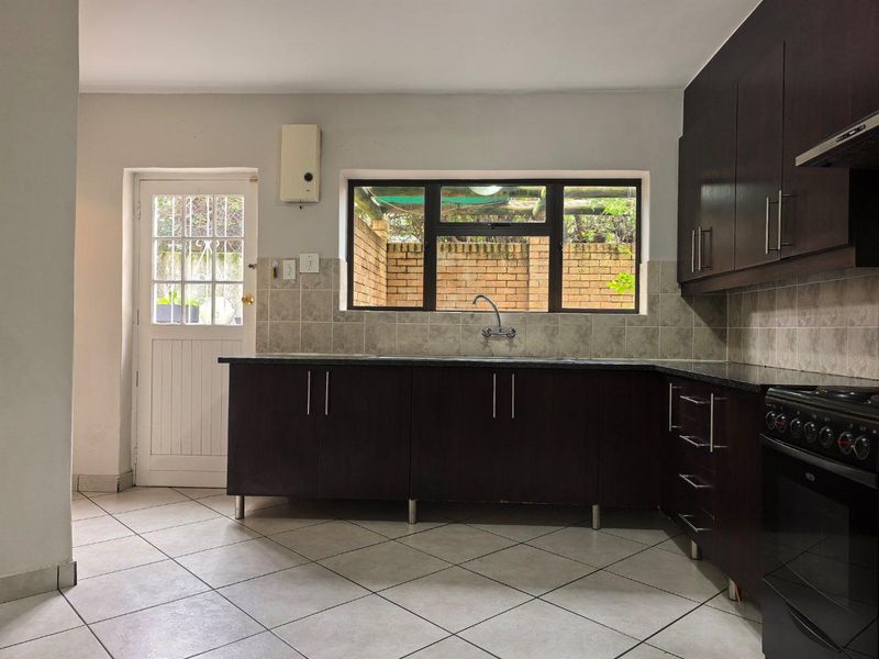 A functional kitchen featuring dark wood cabinetry, granite countertops, tiled backsplash, and built-in appliances, with direct access to an outdoor area.