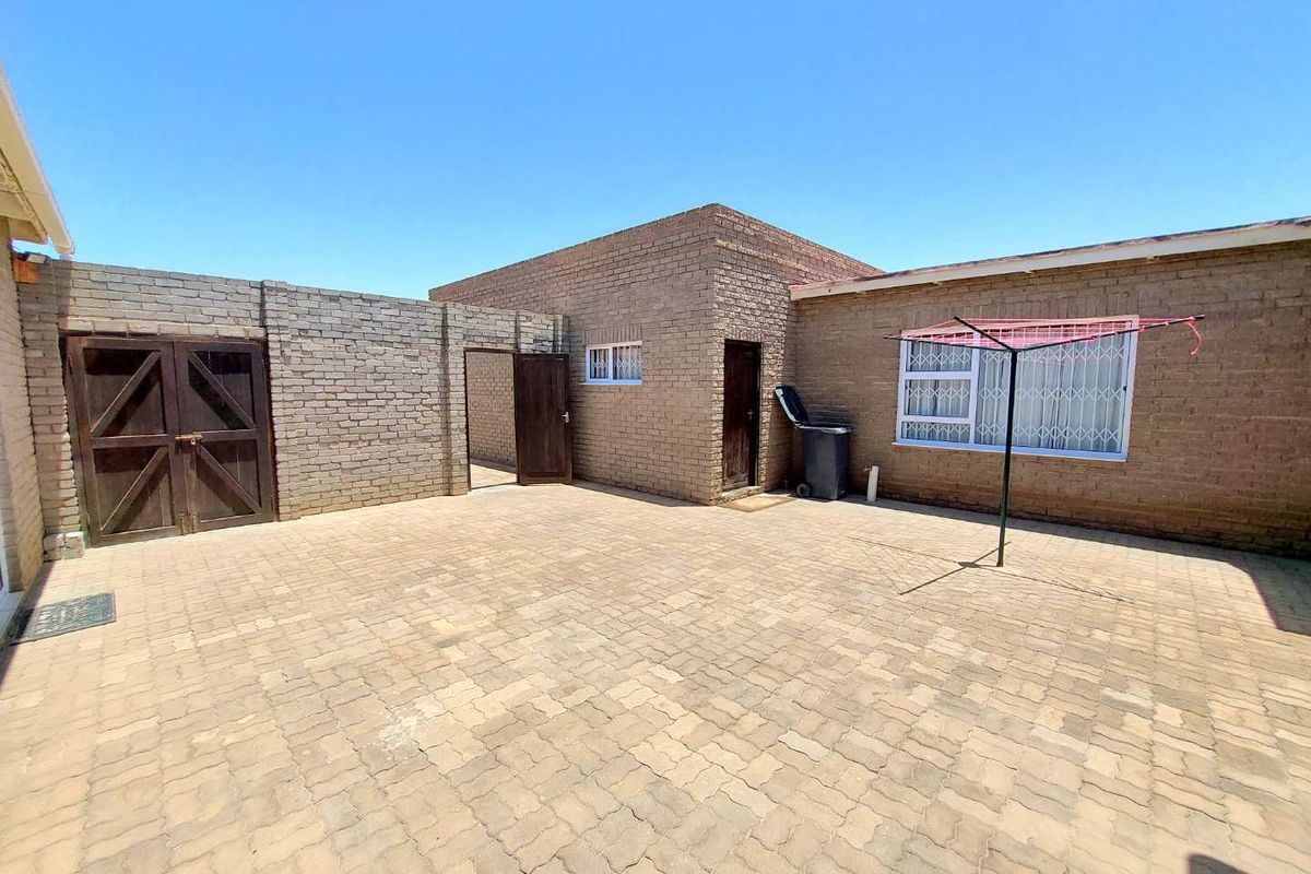 A paved rear courtyard area featuring exposed brick walls, secure metal gates, and security bars on the windows.