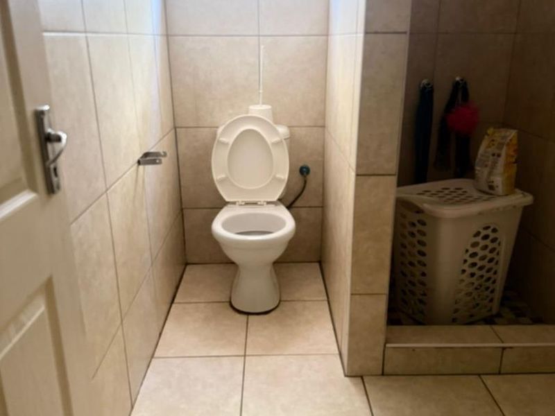 A functional bathroom featuring tiled walls and flooring, a standard toilet, and a small window for natural light.
