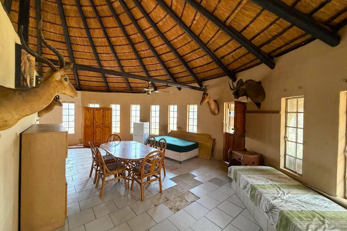 Spacious living area featuring a traditional thatched roof with exposed timber rafters, ceramic tile flooring, and multiple casement windows providing natural light.