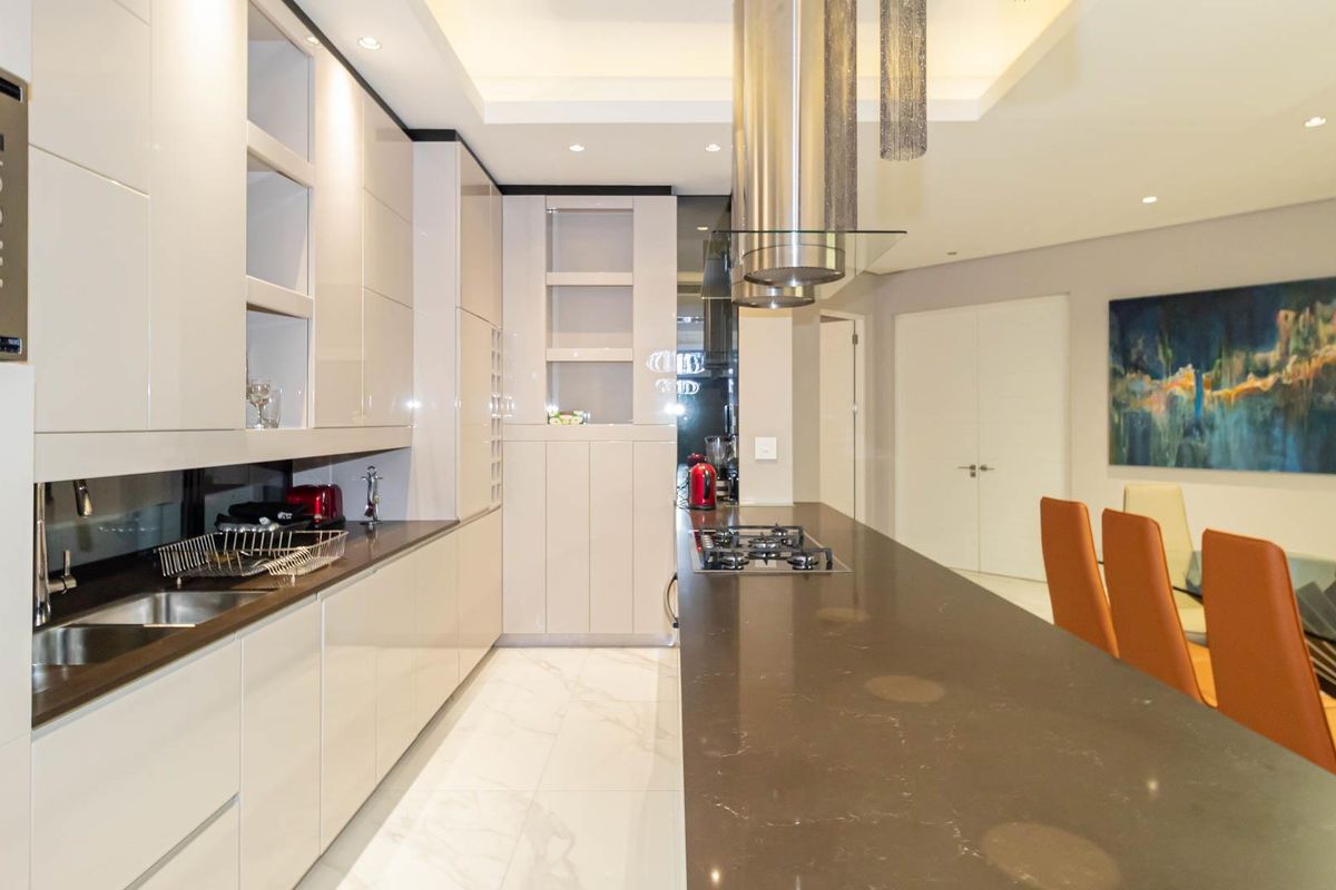 Modern kitchen featuring high-gloss cabinetry, stone countertops, integrated stainless steel appliances, and a breakfast bar island with a built-in gas hob.