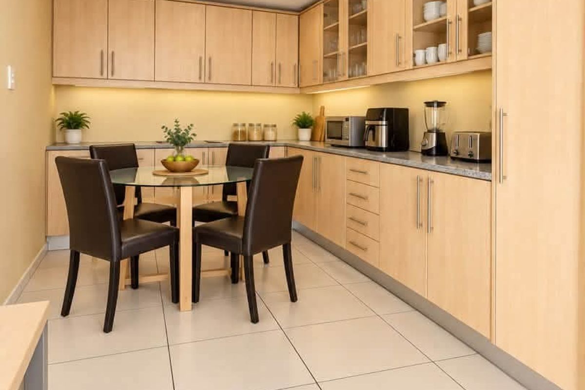 A well-maintained kitchen featuring light-wood cabinetry, stone-look countertops, under-cabinet lighting, and modern tiled flooring, offering a clean and functional workspace.