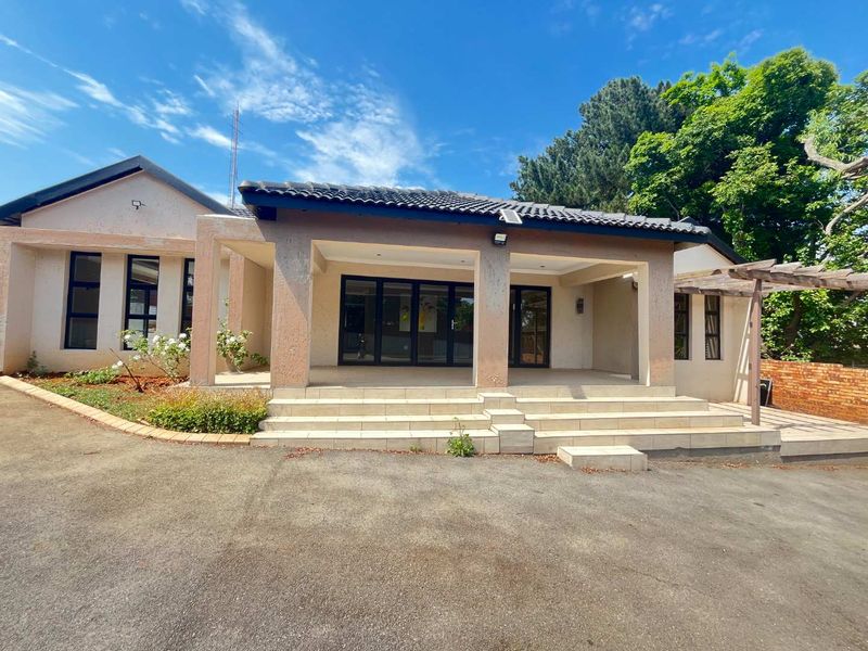 Rear view of the property featuring a spacious tiled patio, concrete driveway, and a timber pergola set against a landscaped garden area.