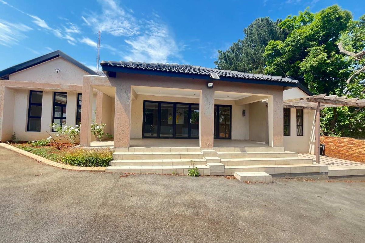 Rear view of the property featuring a spacious tiled patio, concrete driveway, and a timber pergola set against a landscaped garden area.
