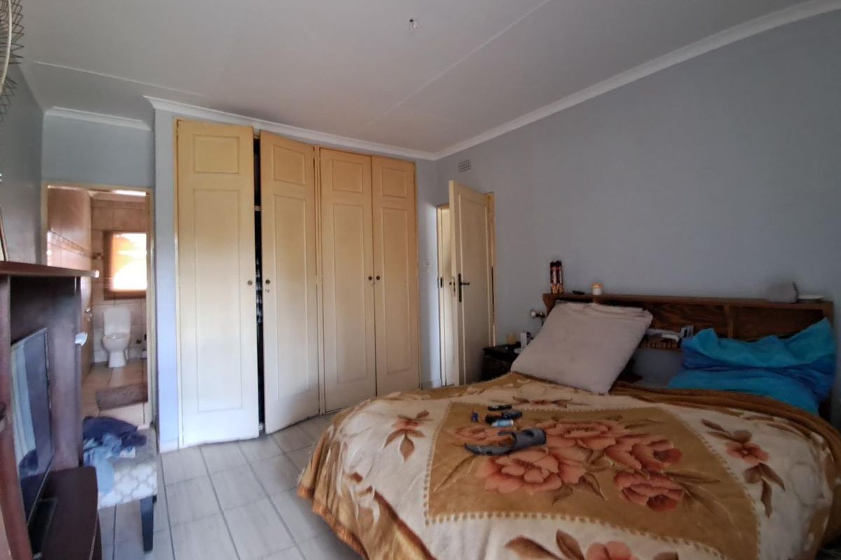 A bedroom featuring built-in wooden cupboards, tiled flooring, and an adjoining en-suite bathroom.