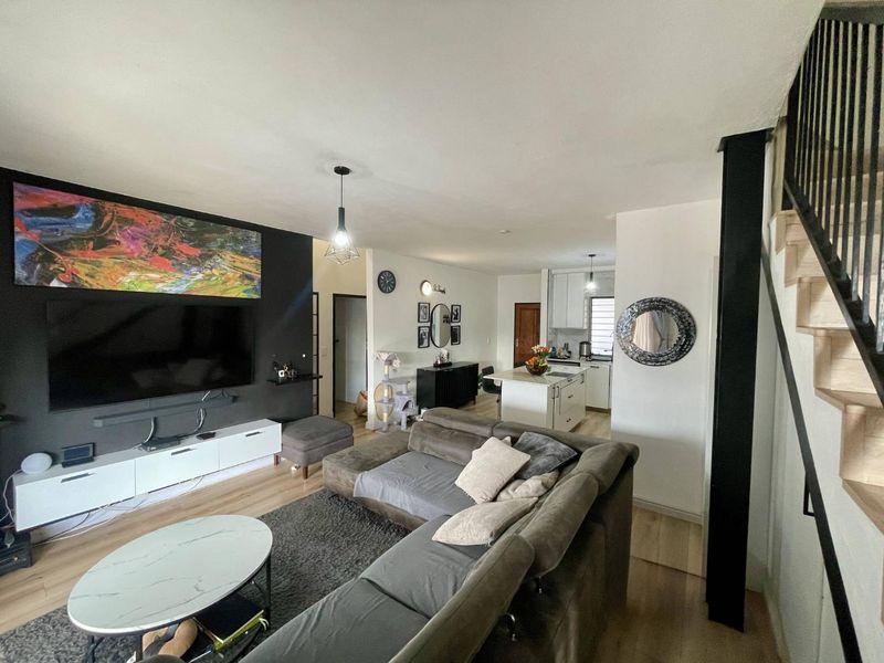 Open-plan living area featuring a modern kitchen with an island, laminate flooring, and a staircase leading to the upper level.