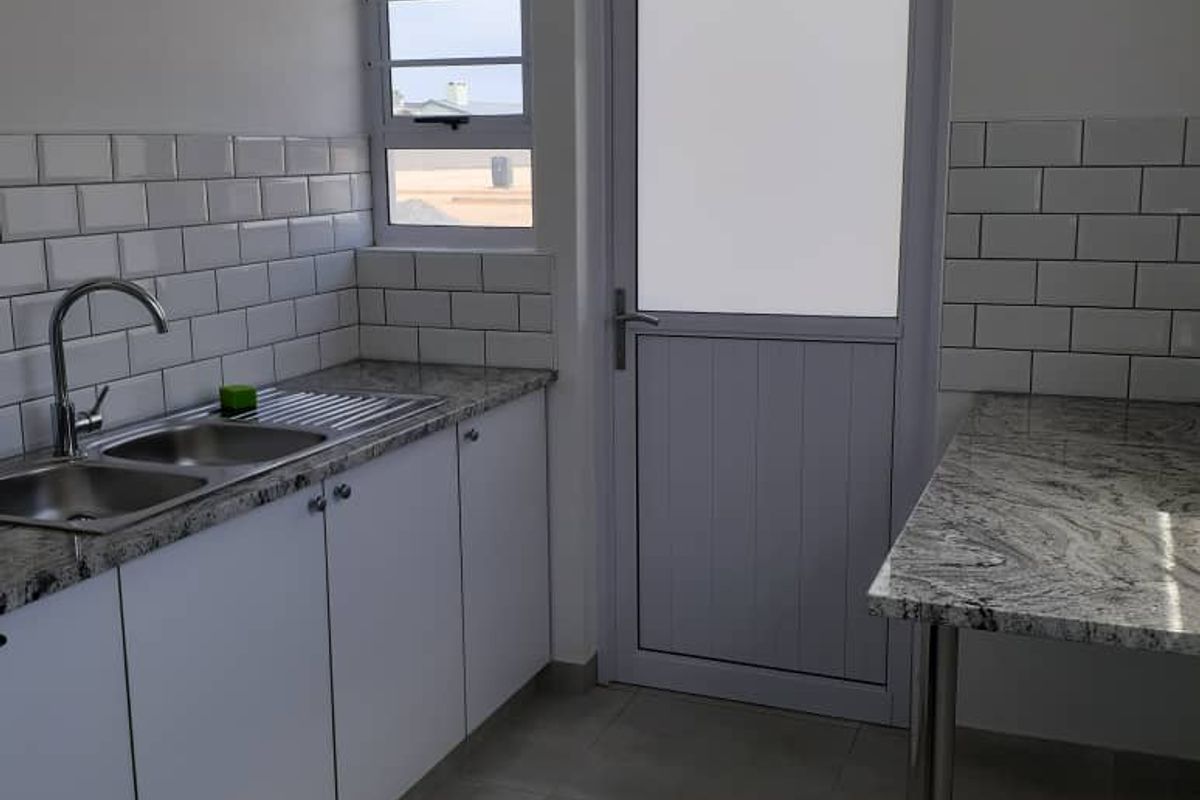 A clean, modern kitchen featuring granite countertops, white cabinetry, subway tile backsplash, and a stainless steel double sink with a side door.