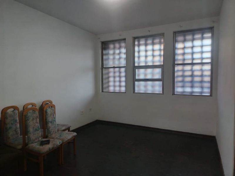 A simple living area featuring dark flooring and windows fitted with security bars, offering a blank canvas for potential interior updates.