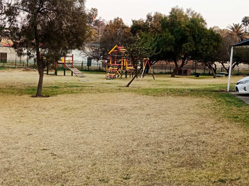 A communal garden area featuring established trees, perimeter fencing, and playground equipment for residents.