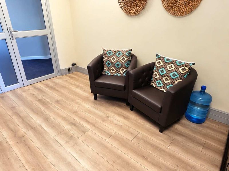 A bright office reception area featuring light wood-look laminate flooring and a modern double glass door entrance.