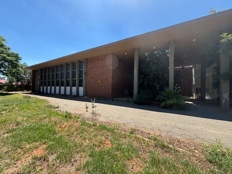 Exterior view of a commercial office building featuring a brick facade, large windows, and a covered walkway with concrete pillars.