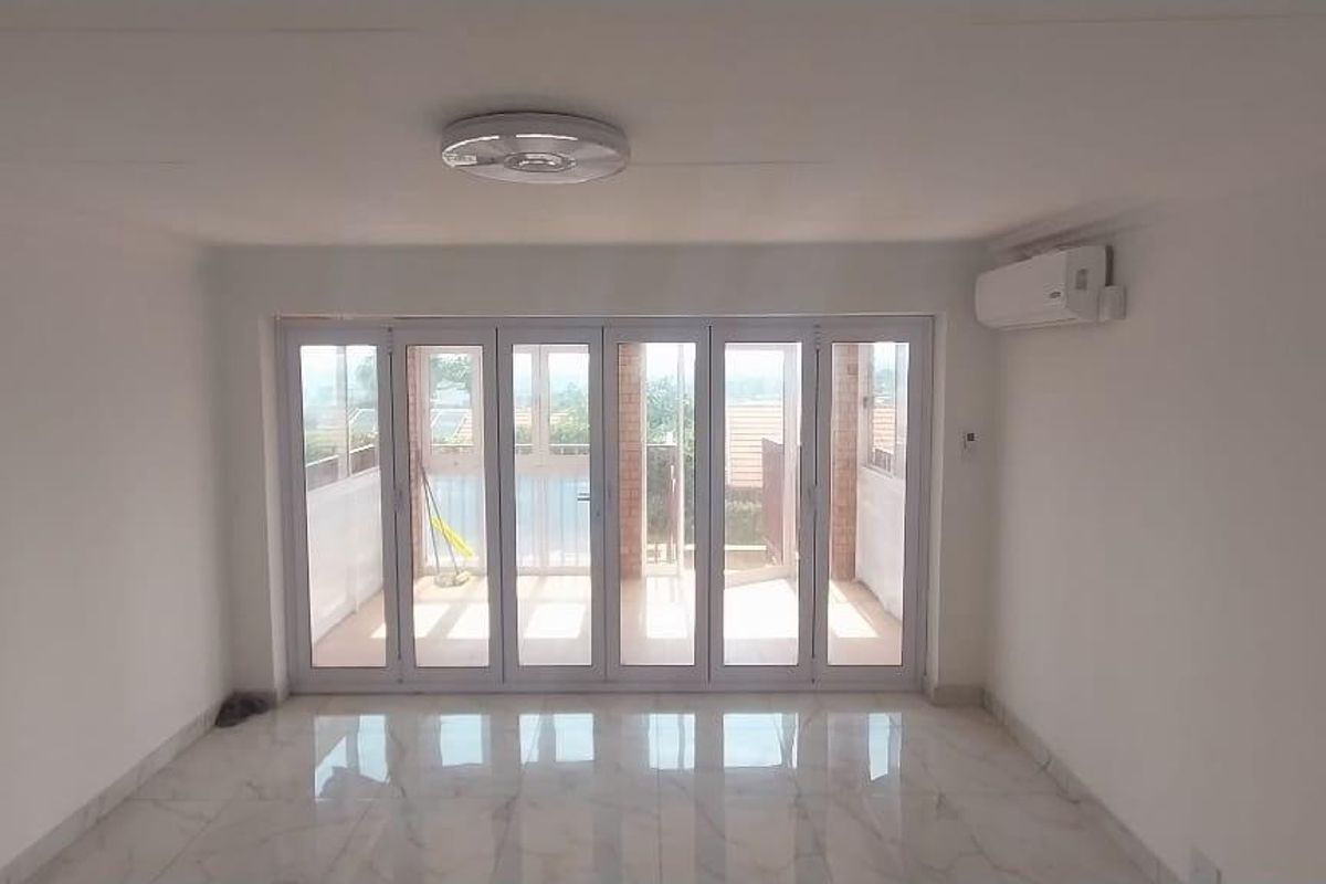 Bright and spacious living area featuring polished marble-look floor tiles, a wall-mounted air conditioning unit, and large glass folding doors leading to a balcony.