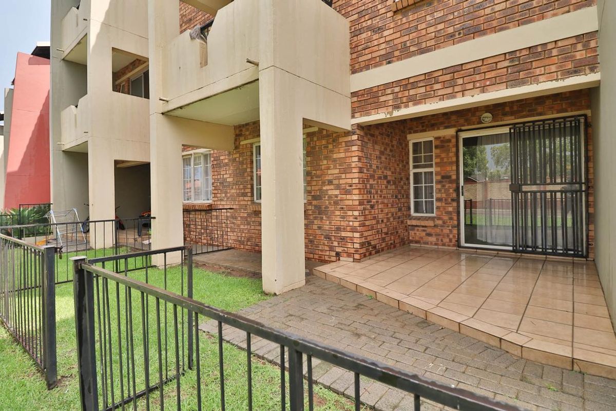 Ground floor apartment exterior featuring a private tiled patio, brick facade, and a small enclosed garden area with metal fencing.