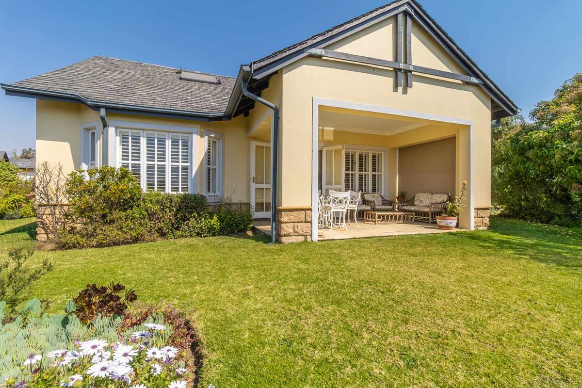 Rear view of the retirement village residence featuring a covered patio, stone base detailing, and well-maintained landscaped garden.