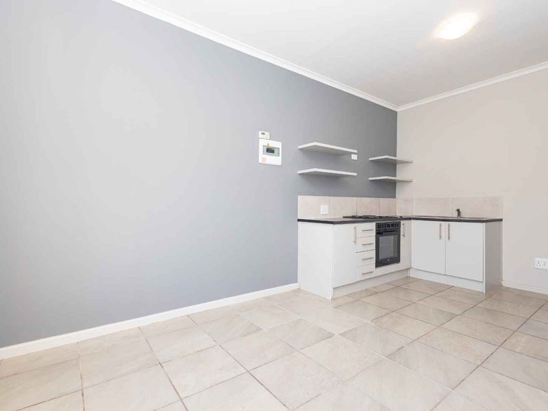 An open-plan living and kitchen area featuring tiled floors, modern grey accent wall, built-in oven, gas hob, and minimalist cabinetry.