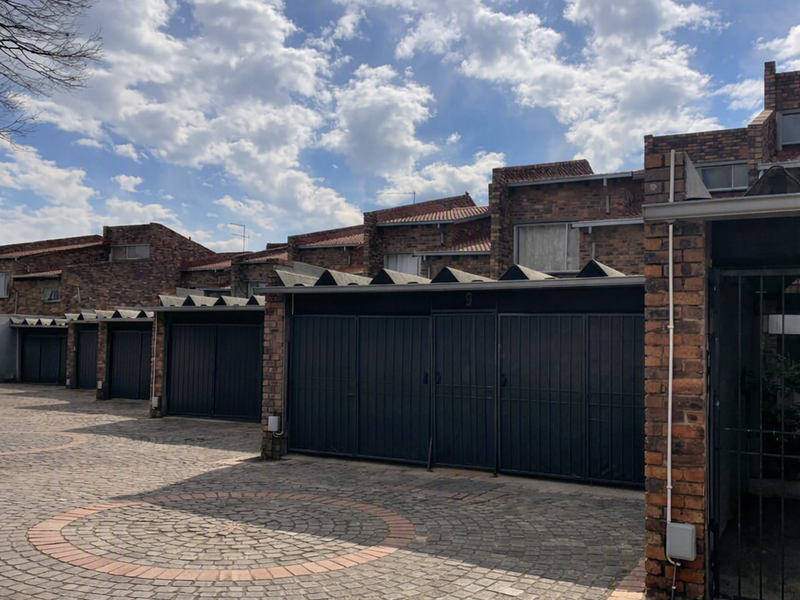 Front exterior view of a townhouse complex featuring brick facades, metal garage doors, and a paved cobblestone driveway.