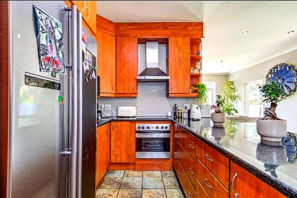 A functional kitchen featuring warm-toned wooden cabinetry, dark granite countertops, a built-in oven, and a stainless steel extractor fan.