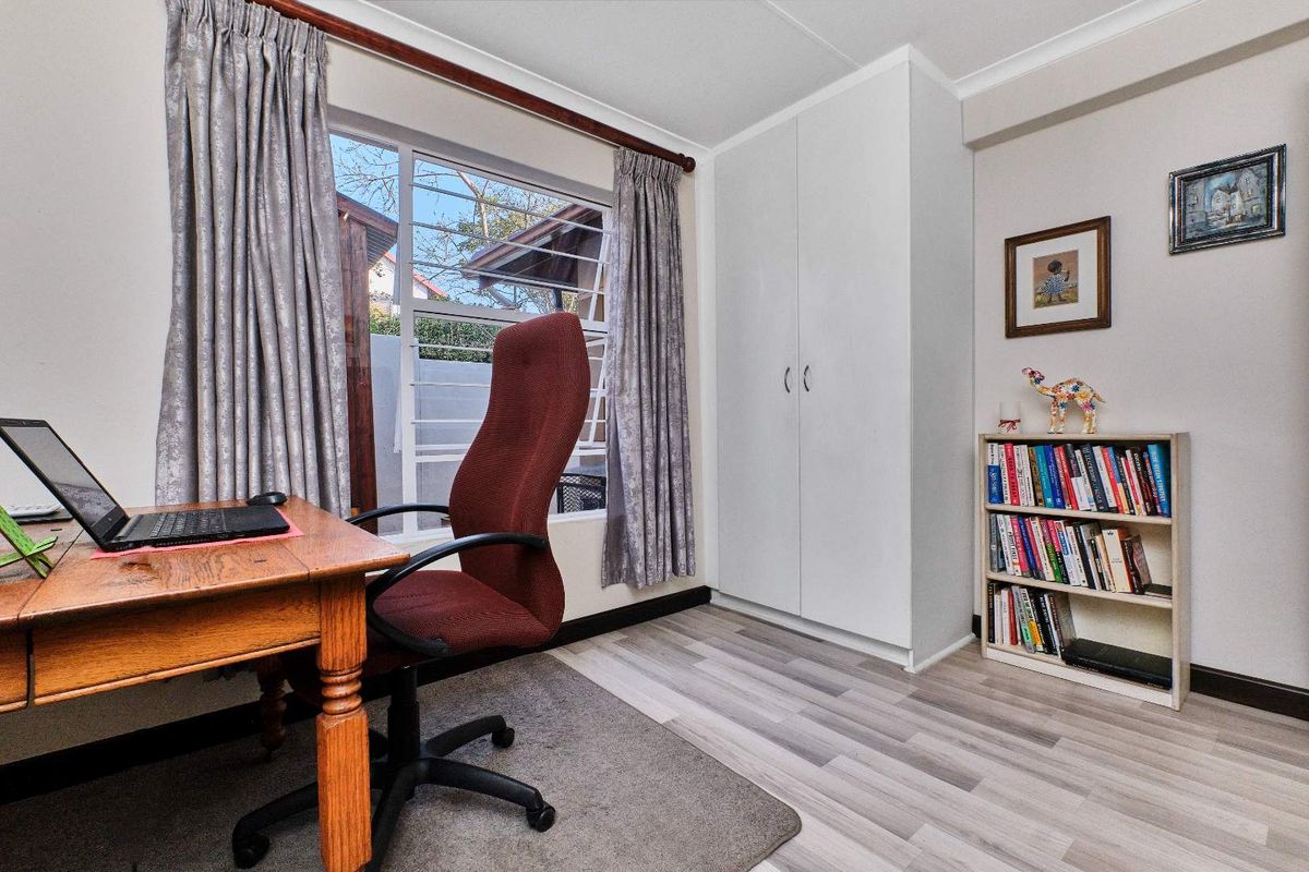 A functional bedroom featuring light-toned laminate flooring, a built-in wardrobe, and a window with security bars, providing a clean and practical living space.