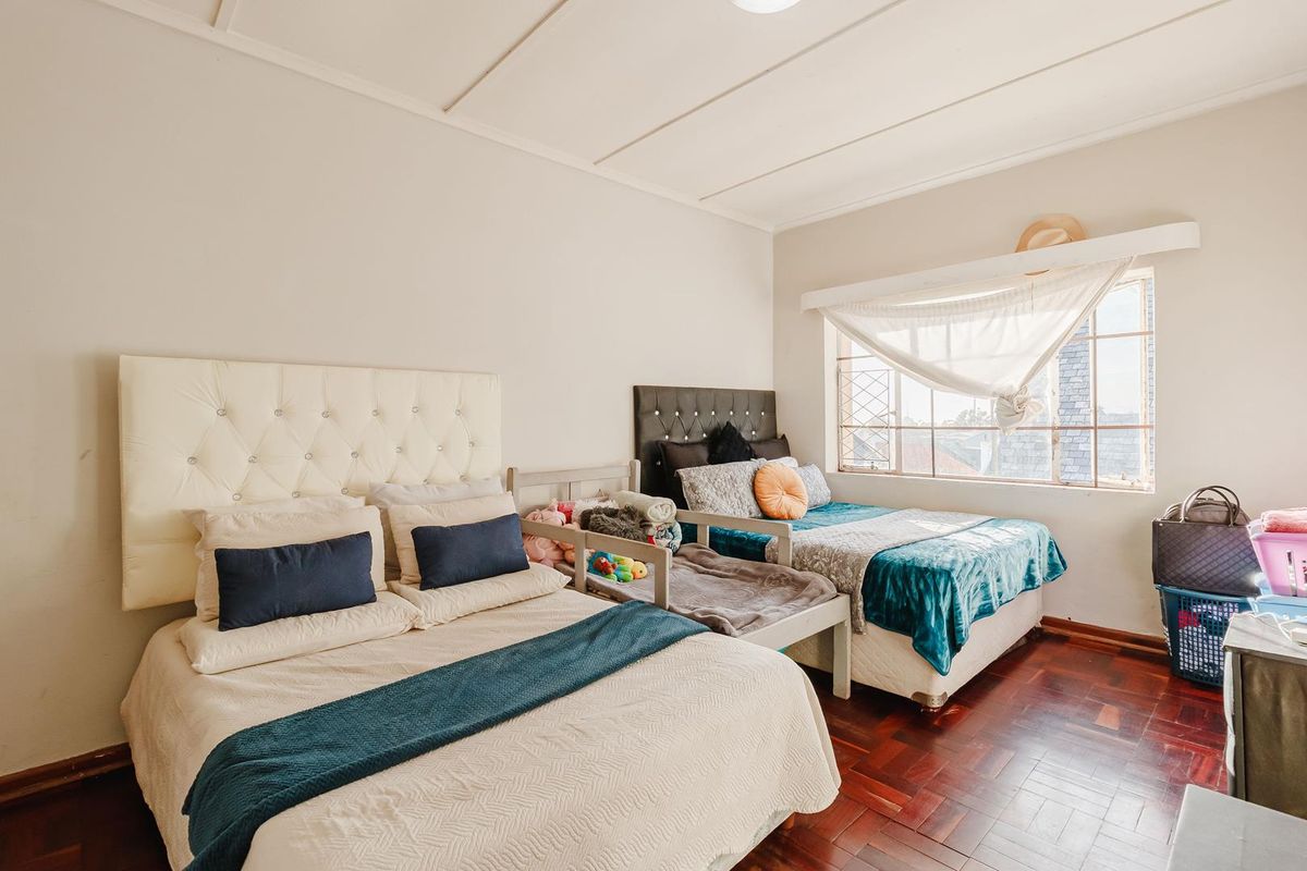 A bedroom featuring warm parquet flooring, a panelled ceiling, and a window fitted with security bars, providing natural light.