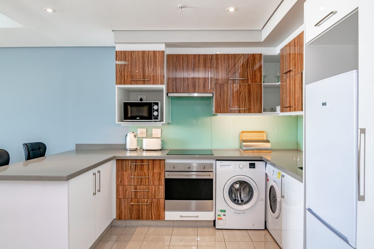 Modern kitchen featuring wood-grain cabinetry, stone countertops, integrated oven, hob, extractor fan, and built-in laundry appliances.