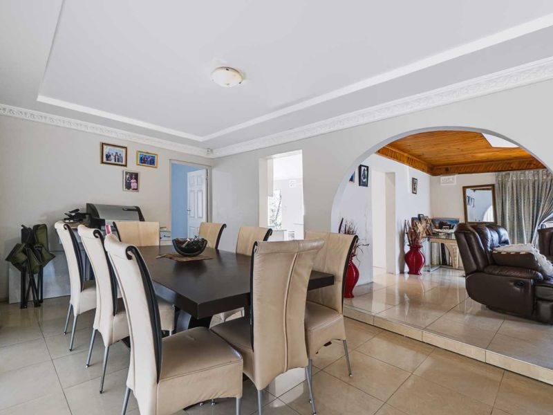 Open plan dining area featuring tiled flooring, decorative crown molding, and a large archway leading into an adjacent living space.