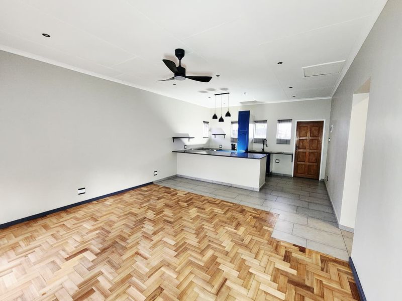 Spacious open-plan living and kitchen area featuring a combination of herringbone parquet and ceramic tile flooring, modern lighting, and a functional kitchen island.