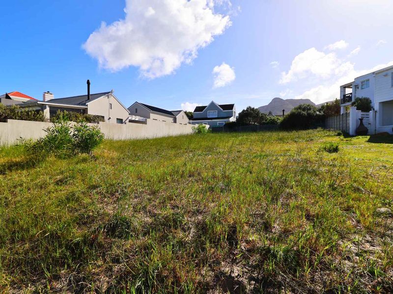 A vacant residential plot featuring natural grass coverage, enclosed by boundary walls and fencing, situated in a developed neighborhood with mountain views.