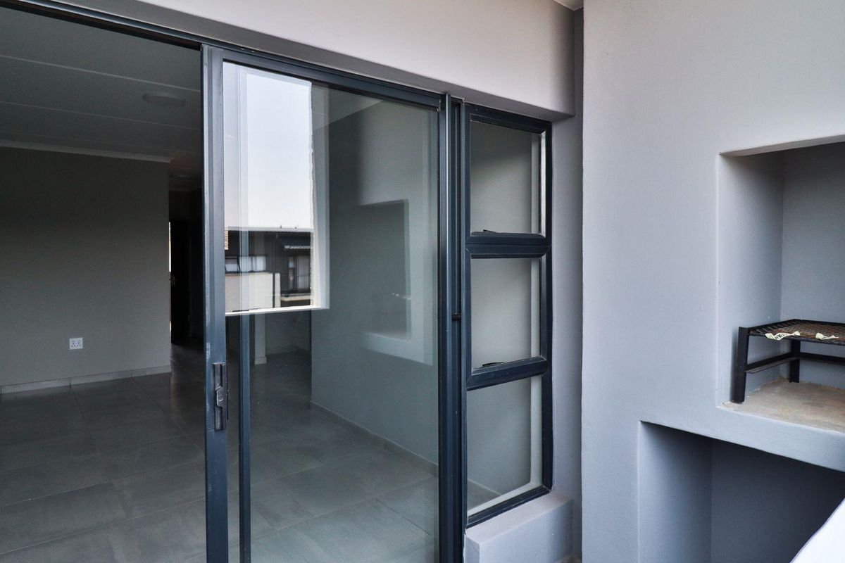 A clean, modern balcony featuring tiled flooring, a built-in braai, and large sliding glass doors providing access to the interior living space.