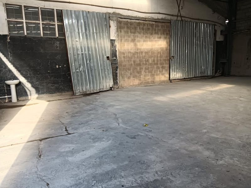 Spacious industrial utility area featuring a concrete floor, large corrugated metal sliding doors, and a wall-mounted pedestal sink.