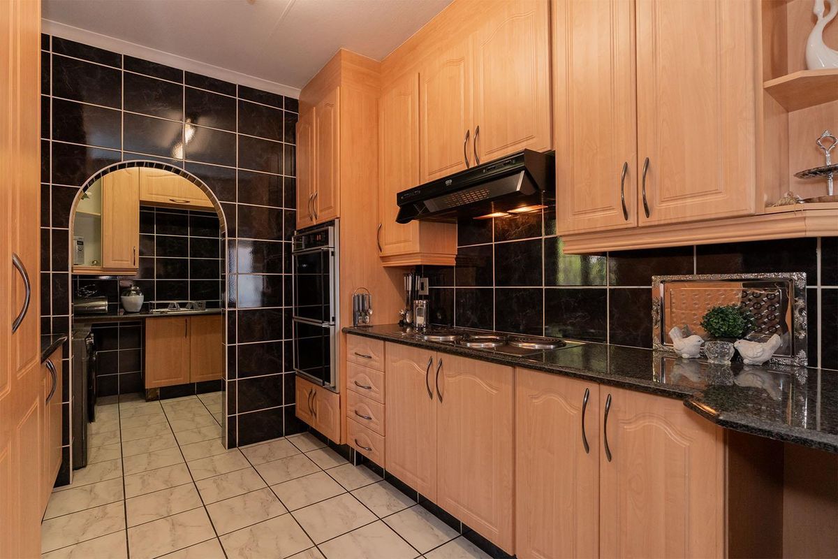 A functional kitchen featuring light wood cabinetry, dark granite countertops, black tiled splashbacks, and a built-in oven with an extractor fan.