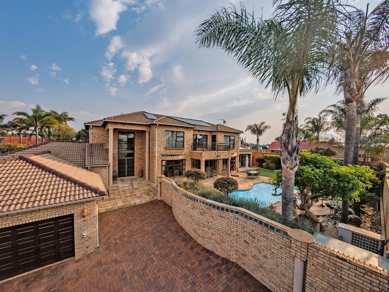 A spacious double-story brick residence featuring a swimming pool, paved driveway, balcony, and well-maintained garden area.