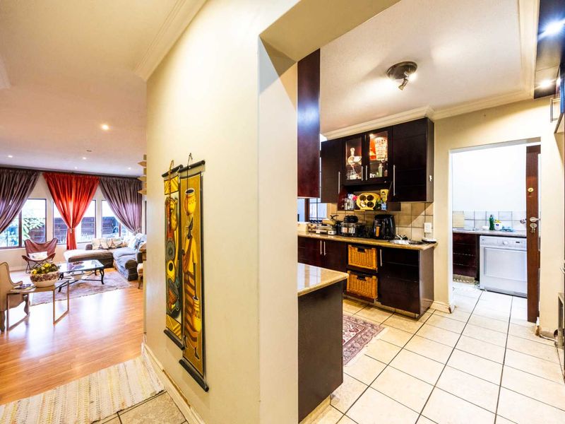 Open plan living area featuring a kitchen with dark wood cabinetry, granite countertops, and an adjoining scullery with tiled flooring throughout.