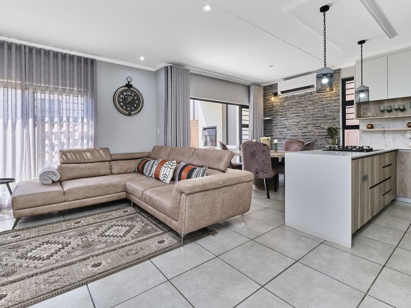 Modern open-plan living area featuring a sleek kitchen with island, stone-clad feature wall, tiled floors, and seamless flow to the outdoor patio.