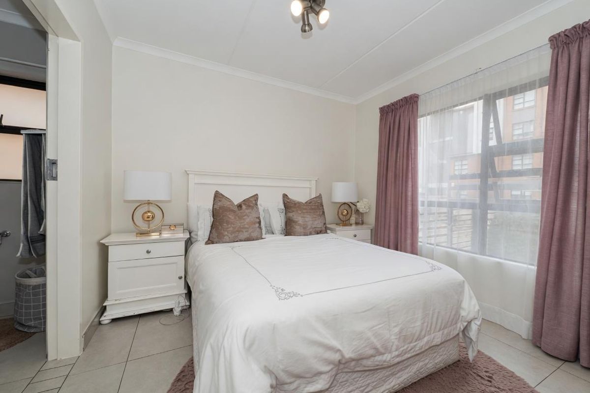 A well-maintained bedroom featuring tiled flooring, a large window with curtain tracks, and a ceiling-mounted light fixture.