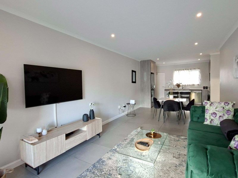An open-plan living and dining area featuring modern tiled flooring, recessed downlights, and a seamless transition into a functional kitchen space.