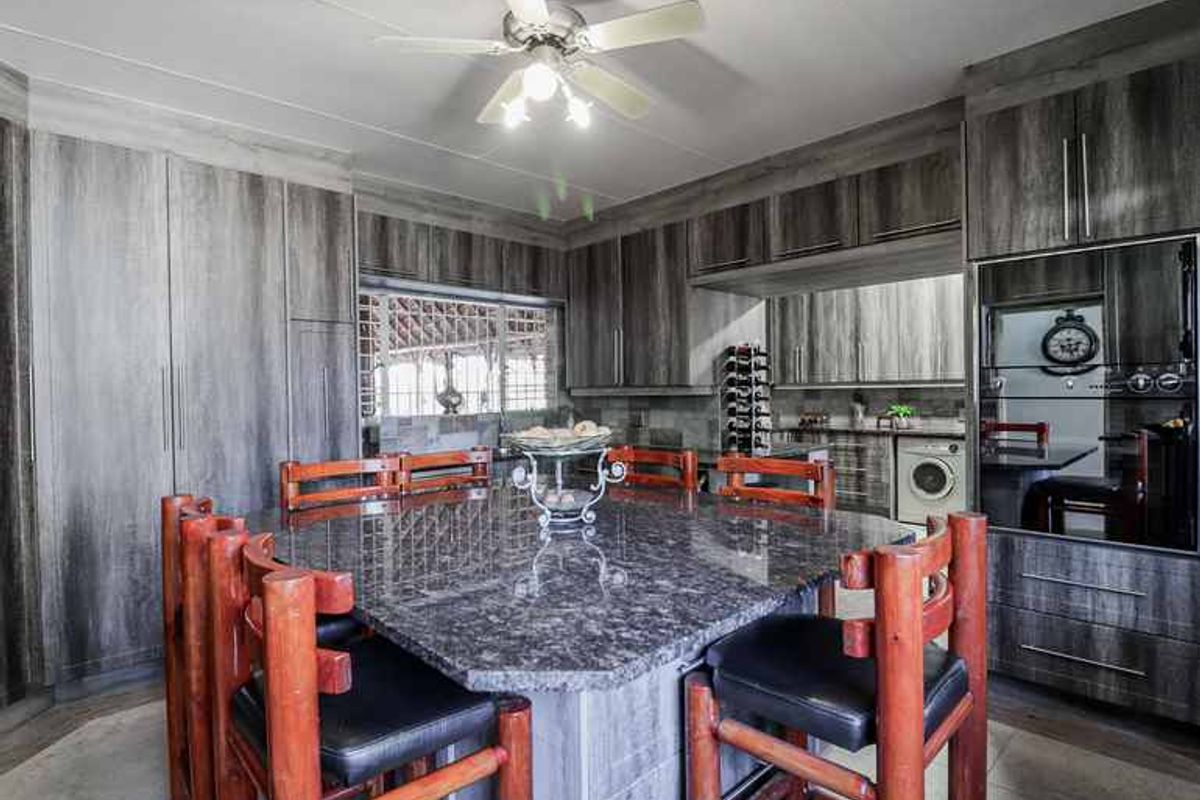 Modern kitchen featuring a large granite-topped island, extensive laminate cabinetry, built-in oven and microwave, and a functional ceiling fan.