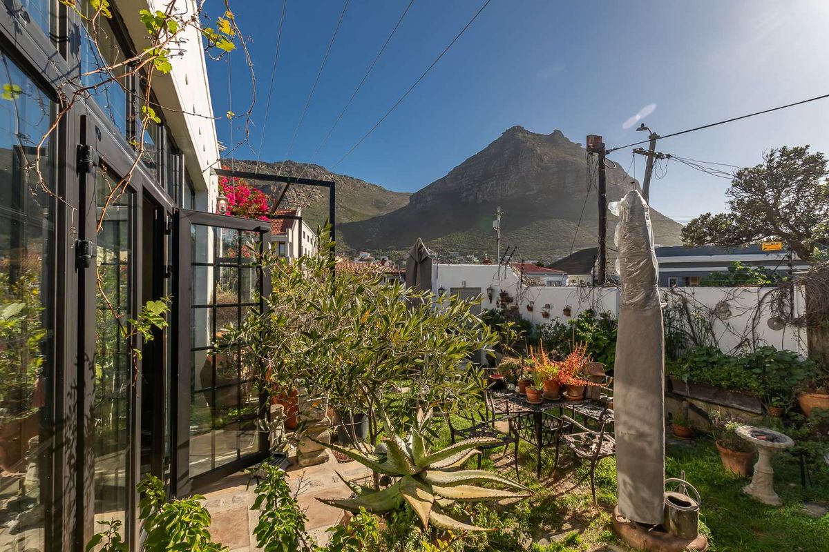 A private rear garden featuring a stone-paved patio area with direct access through black steel-framed glass doors, set against a scenic mountain backdrop.