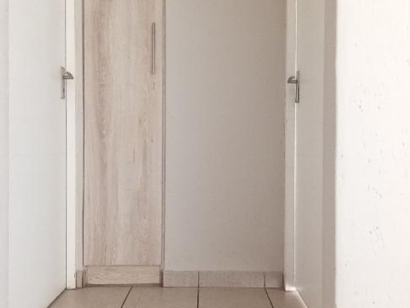 A clean, neutral hallway featuring tiled flooring and a tall built-in cupboard, providing functional storage space within the home.