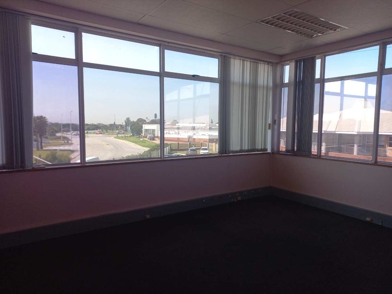 An empty office space featuring large windows with vertical blinds, recessed ceiling lighting, and carpeted flooring, offering ample natural light and exterior views.
