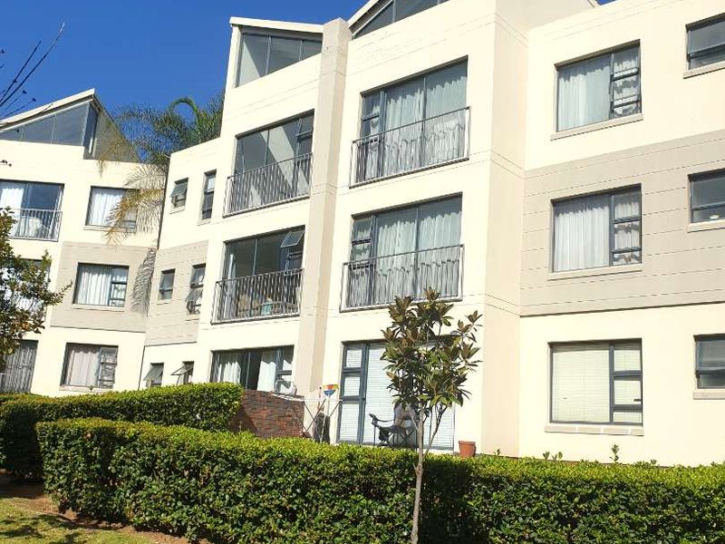 Exterior view of a multi-story apartment building featuring balconies, large sliding glass doors, and well-maintained landscaped garden areas.