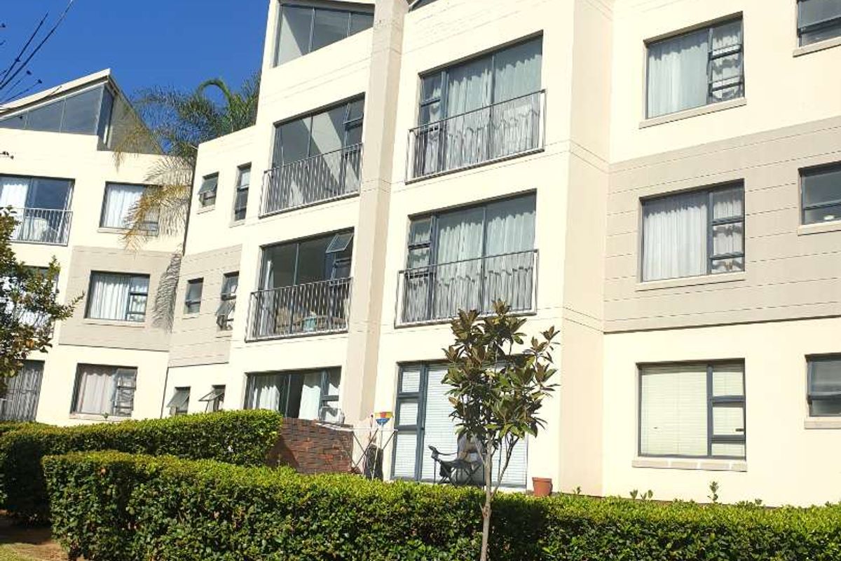 Exterior view of a multi-story apartment building featuring balconies, large sliding glass doors, and well-maintained landscaped garden areas.