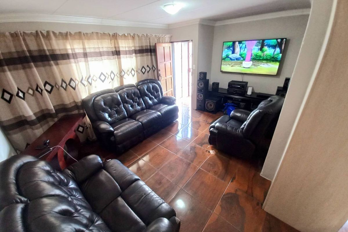 A living room featuring polished dark-toned floor tiles, neutral wall finishes, and a wall-mounted television setup.
