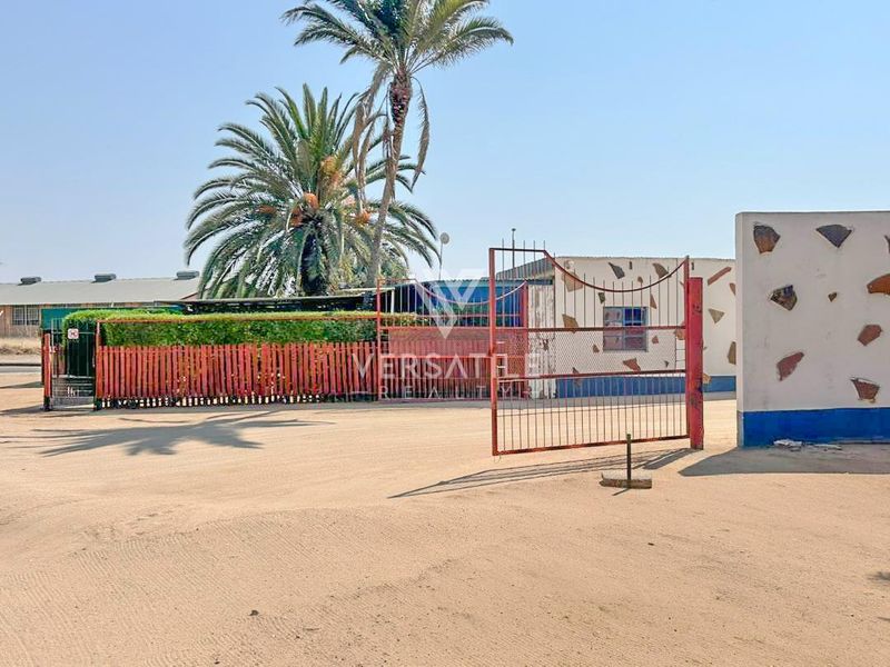 Front exterior view of the industrial property featuring a metal security gate, perimeter fencing, and a concrete boundary wall.