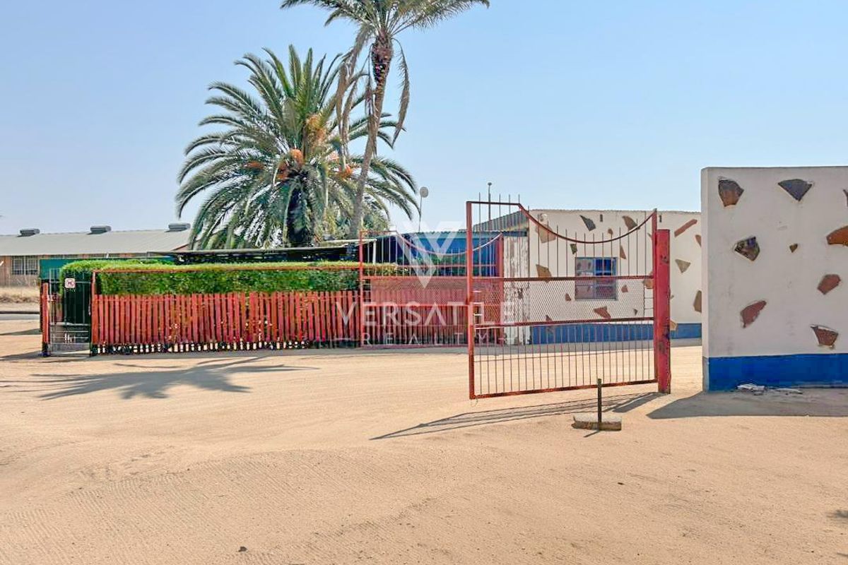 Front exterior view of the industrial property featuring a metal security gate, perimeter fencing, and a concrete boundary wall.