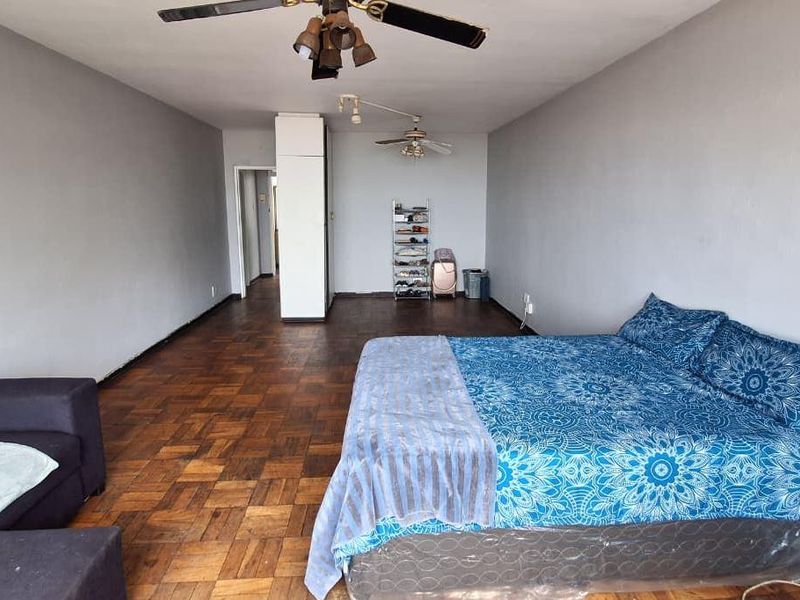 Spacious bedroom featuring classic parquet flooring, dual ceiling fans, and a built-in cupboard, offering a versatile layout for comfortable living.